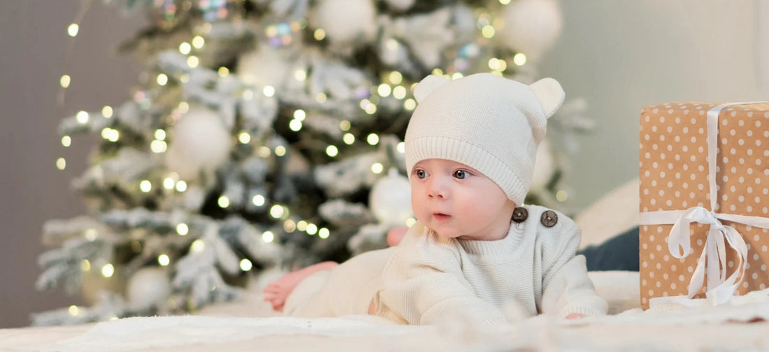 Baby sitting next to Christmas gifts, celebrating their first holiday season with joy and warmth.