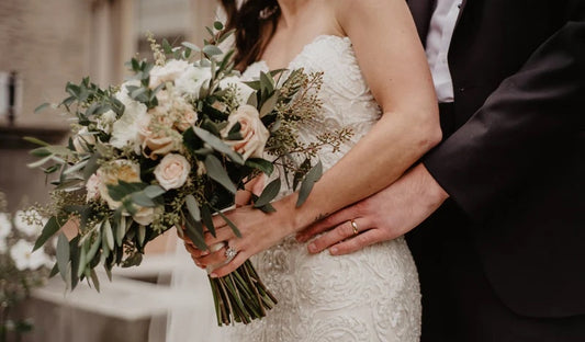 Happy newlywed couple on their wedding day, and holding flowers..