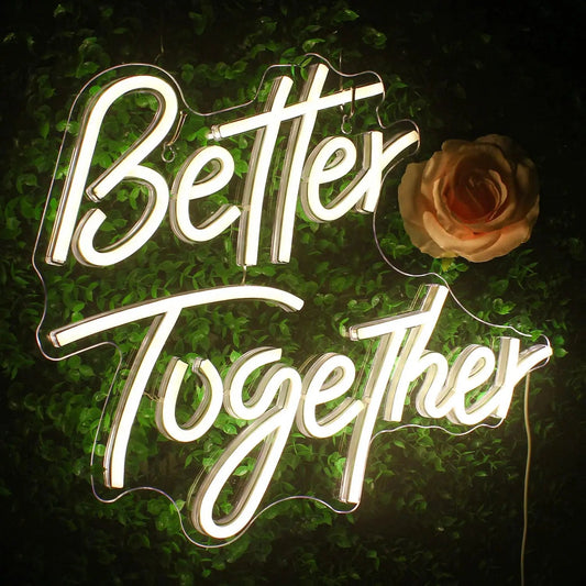 Personalized neon sign displaying the text "Better Together" in white light, set against a backdrop of green leaves.