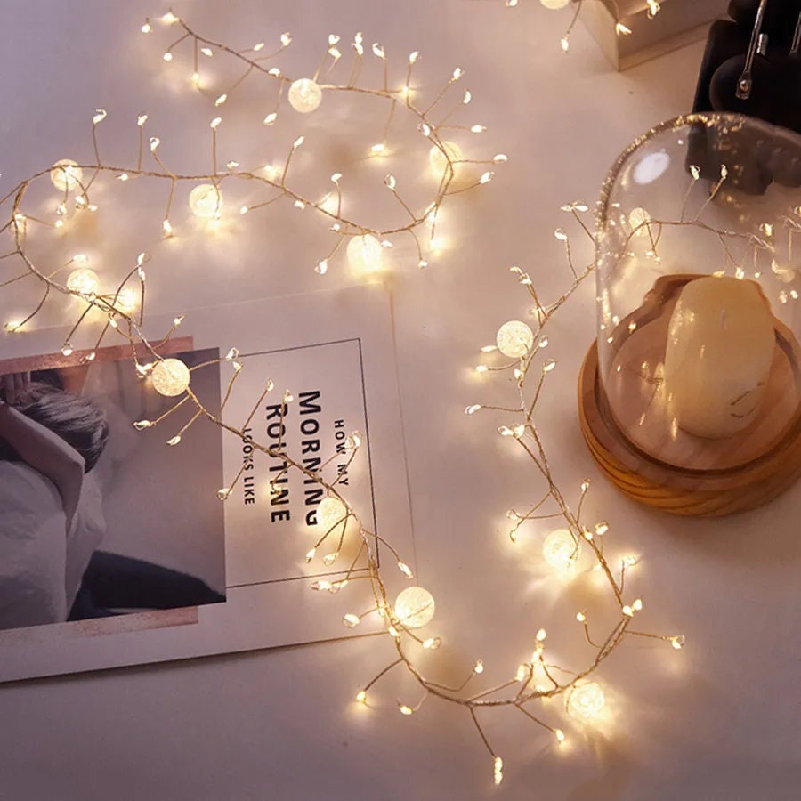 Fairy lights with crackling crystals on a table alongside a glass dome and a magazine, adding a cozy, inviting glow to the space.