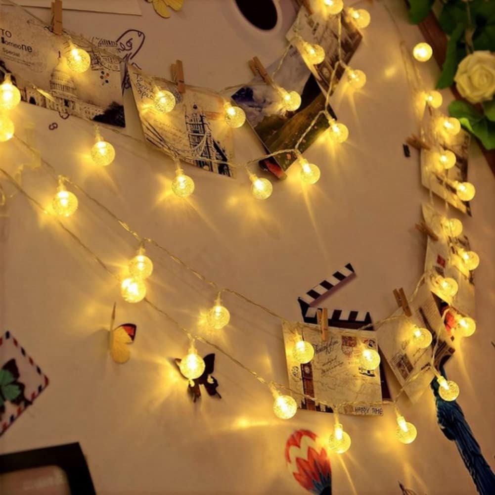 A light chain in the shape of crystal balls hangs on a bedroom wall adorned with pictures.
